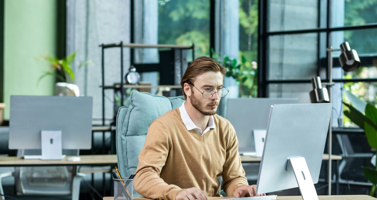 Serious and scorn-centered man in the office at work with a computer, man typing thoughtfully on